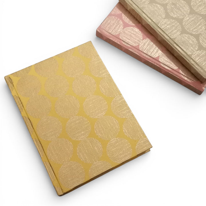 Yellow recycled handmade paper notebook with gold geometric sunrise pattern on a white background