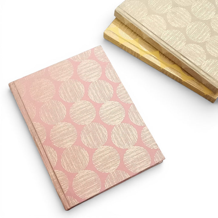 Pink recycled handmade paper notebook with gold geometric sunrise pattern on a white background