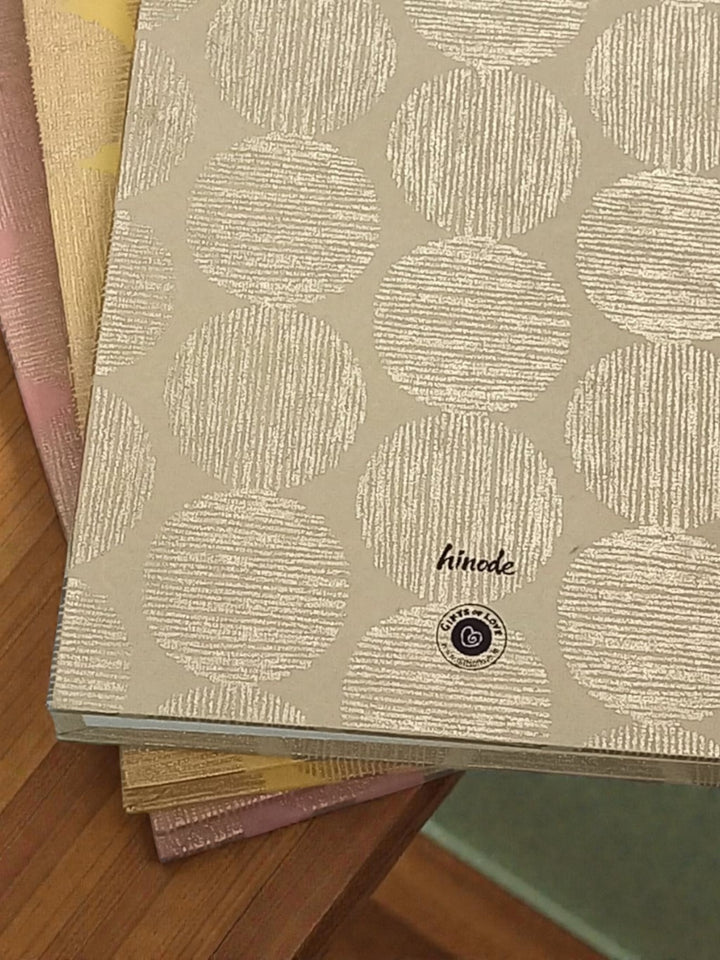 Stack of notebooks with geometric sunrise pattern and branding on a wooden surface