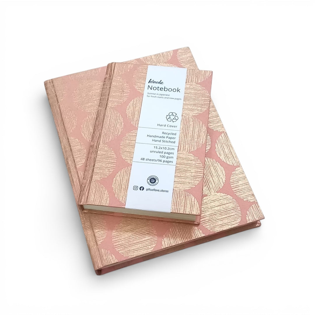 Two notebooks with a pink and gold geometric sunrise pattern on a white background