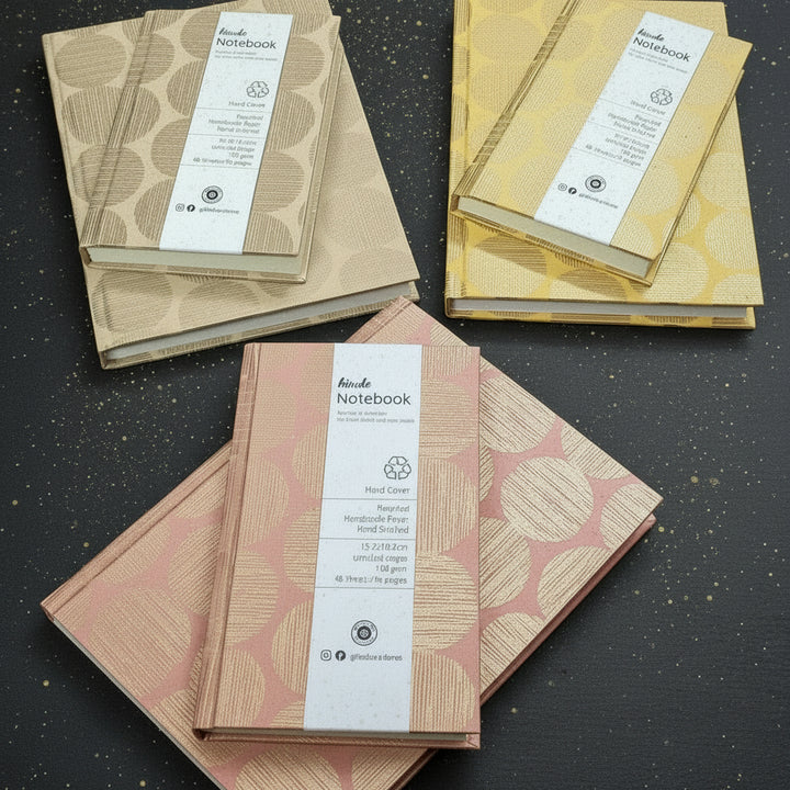 Hardbound Notebooks sustainably made with handmade paper, silk screen printed with the Gifts of Love Hinode design laying flat on a dark background.