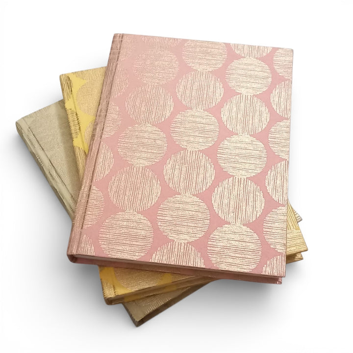 Three notebooks in different colours with the same cover designs stacked on a white background