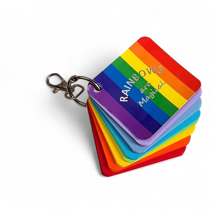 Rainbows are Magical notebook with a stack of rainbow-colored paper and a keychain on a white background.