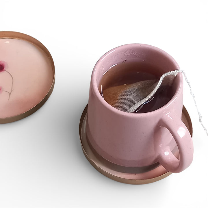 Pink mug with a tea bag on a matching coaster on a white background