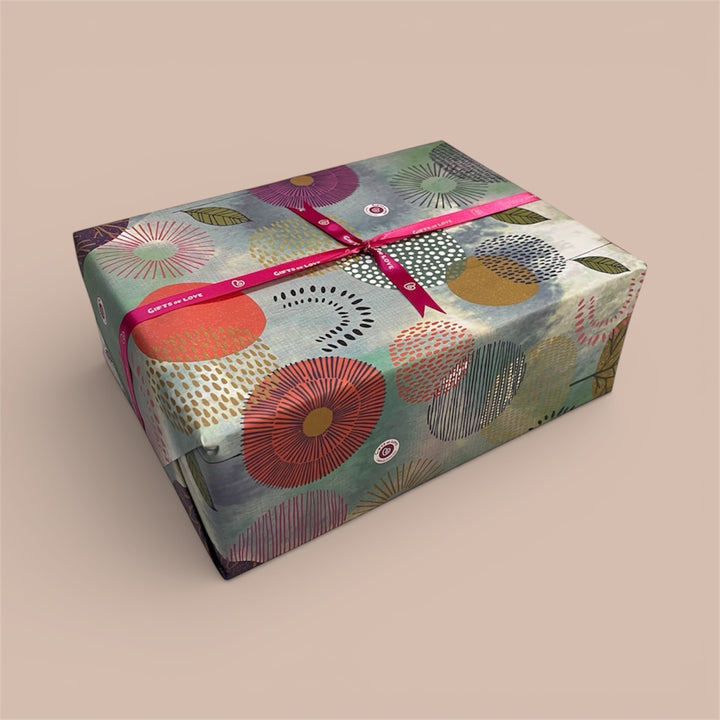 Gift box wrapped in colourful patterned paper with a Gifts of Love branded ribbon on a beige background. 