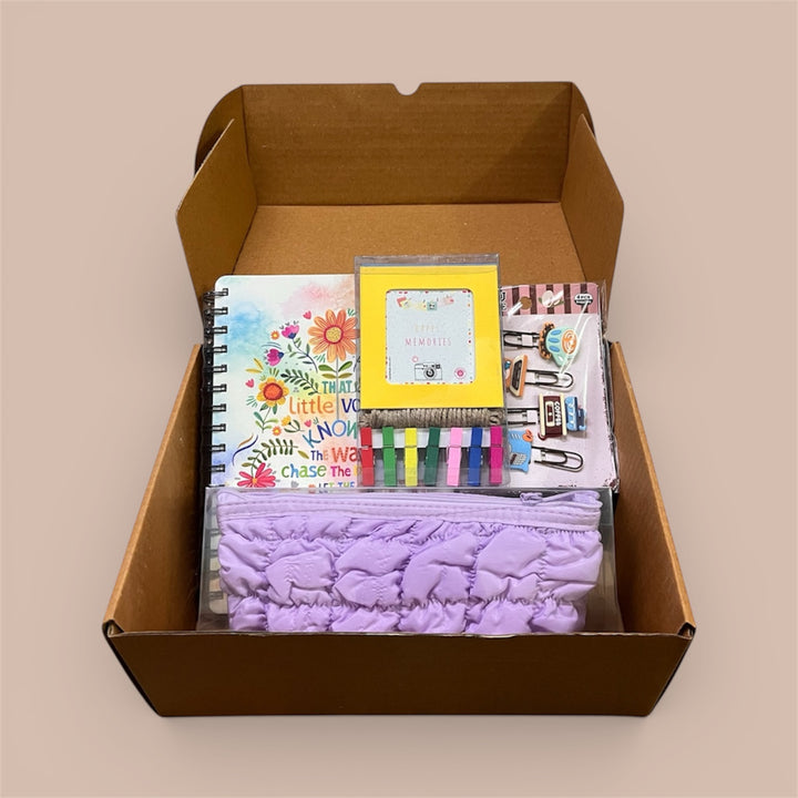 Box containing stationery items including a notebook, pencil pouch, photo holder and other supplies on a beige background