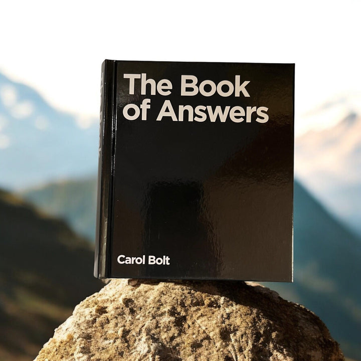 The Book of Answers by Carol Bolt, placed on a rocky surface with a mountainous background.